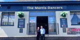 A woman and a man standing together, smiling, outside the Morris Dancers pub in Bolton