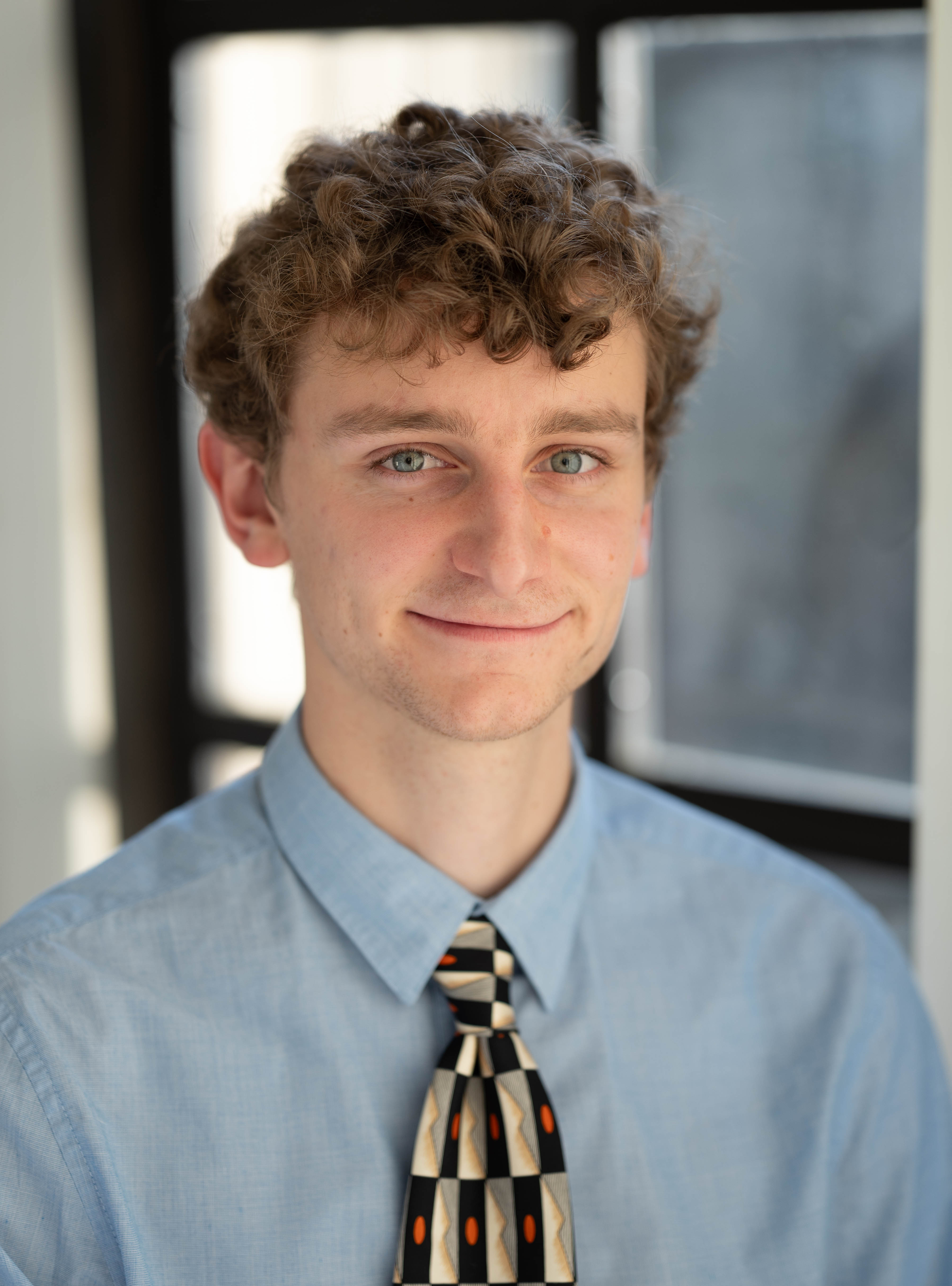 A young man posing for a headshot and smiling at the camera