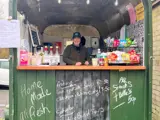 A person standing inside a green converted horsebox. There are snacks and drinks on the counter.