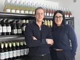 A man and a woman stood side by side. The man has his arms folded and both are wearing black clothes. Behind them are four shelves filled with premium alcohol free beverages