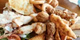 A plate with a small amount of salad on the left, a mixture of chicken goujons, grilled chicken, onion rings and potato wedges