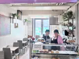 Two people stood behind a cafe counter containing cakes. There is a pink sign above them saying "Mamma Julie's"