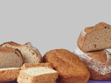 Several loaves of bread, some sliced, piled up for a photo on a purple surface with a white background