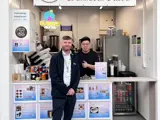 Two men standing at a food counter. One is in front of the counter and one is behind the counter. The man behind the counter is giving a thumbs up.