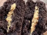 A thick chocolate cookie with a beige coloured filling broken in half