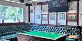 A pool table in a pub with dark green cushioned seating around it