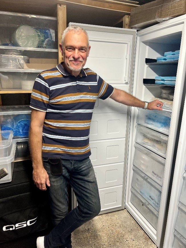 A man smiling, standing by an open freezer