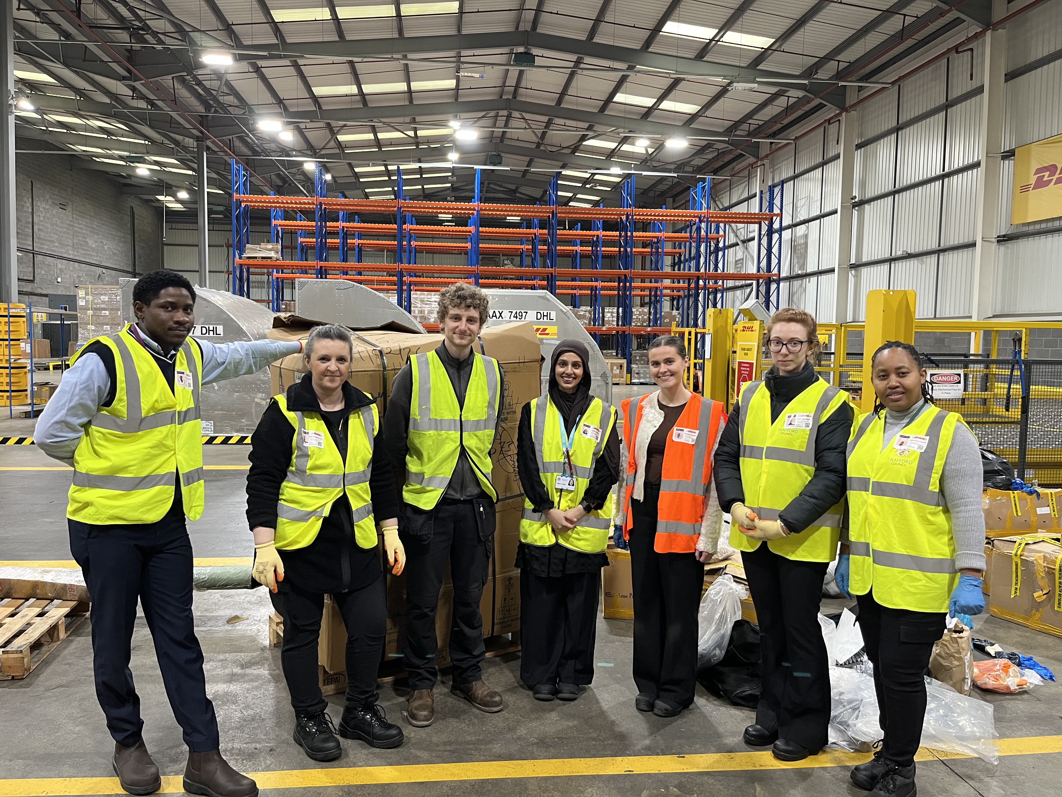 Business Compliance Support officers posing for a photo. They are wearing hi-vis vests and are in a warehouse