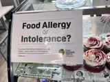 A food allergy notice stuck on the front of a glass cake counter